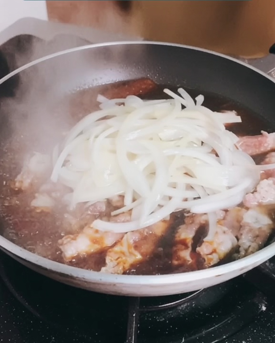 Adding the previously cooked onions back into the pan with the simmering beef.