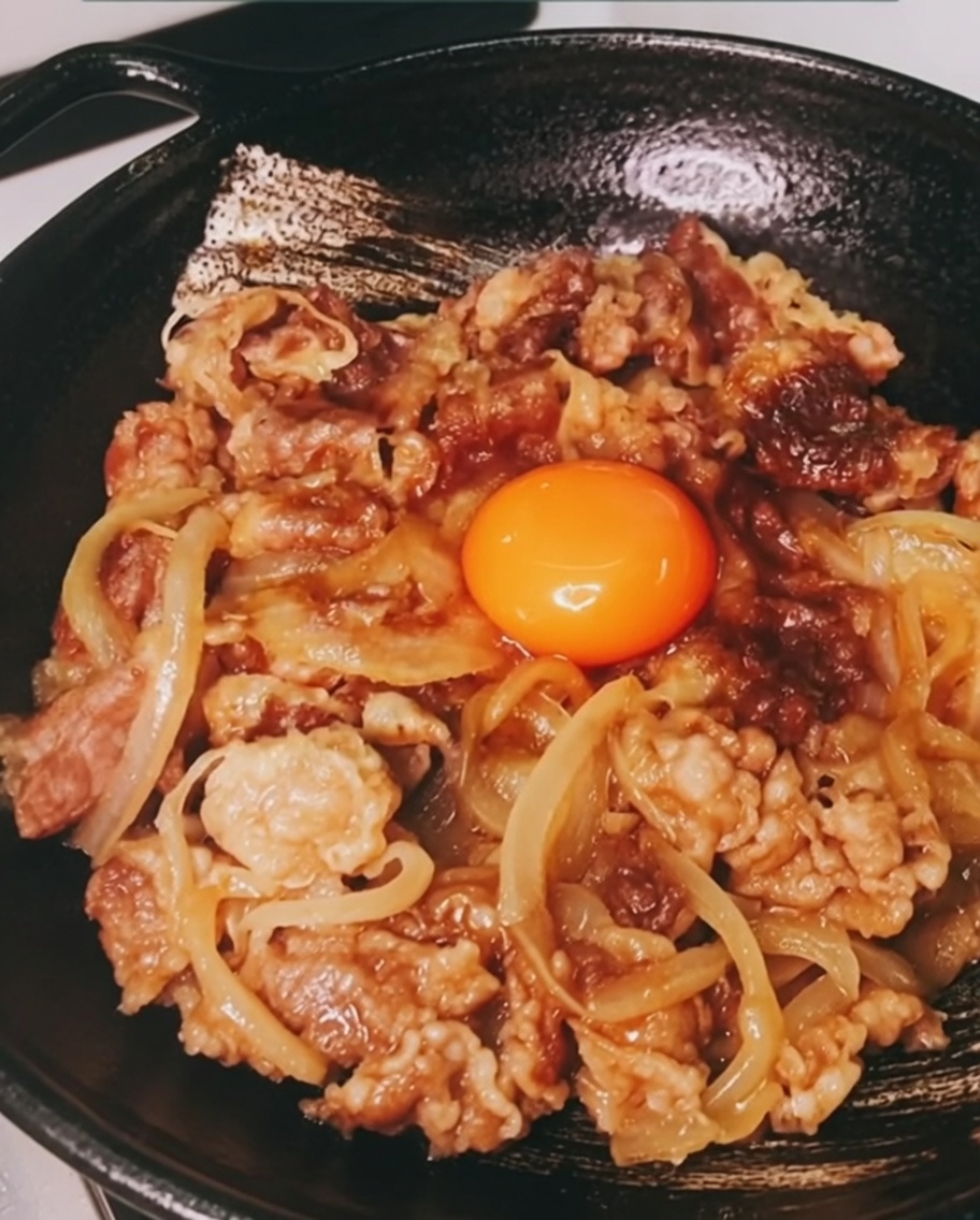 A bright orange raw egg yolk resting in the center of a bed of cooked sliced beef and onions.