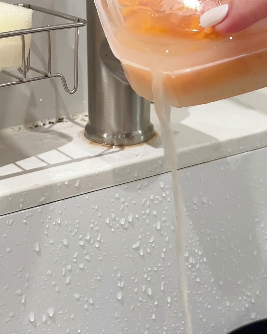 Plastic container of orange sea urchin being tipped over a sink to drain out the liquid.