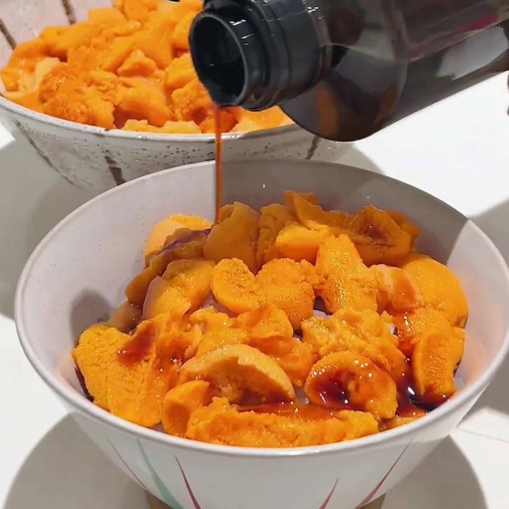 Soy sauce being drizzled from a bottle onto a bowl filled with fresh, bright orange sea urchin.
