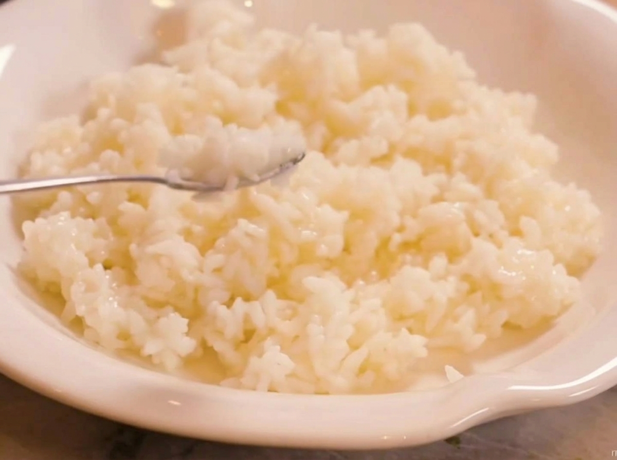 Steamed Thai fragrant rice being combined with sushi vinegar in a white bowl, showing the texture and color of the seasoned rice.