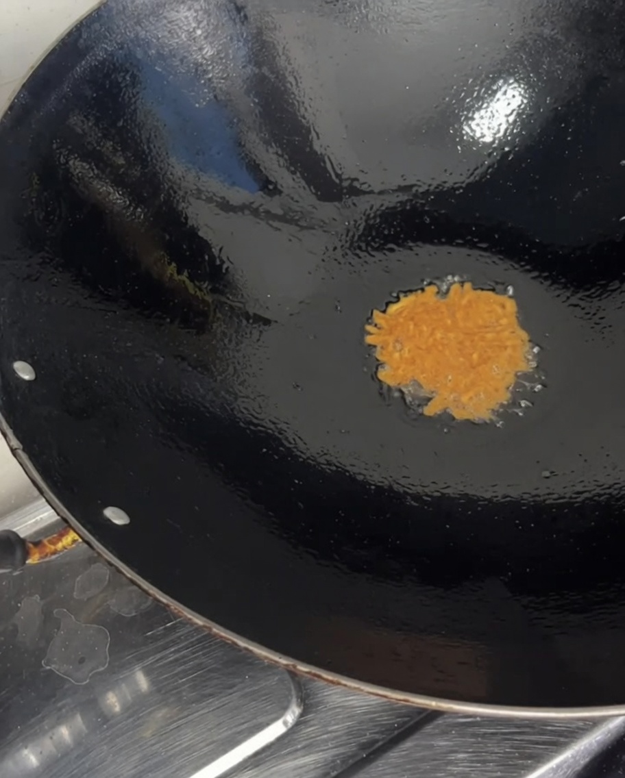 Vibrant orange raw sea urchin roe being poured from a clear bowl into a hot heated wok.