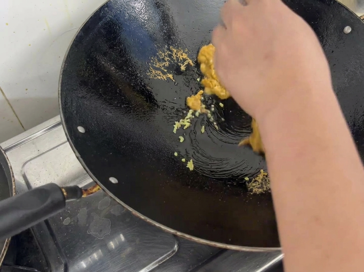 Cooked sea urchin roe crumbled and mixed with minced ginger in a seasoned metal wok.