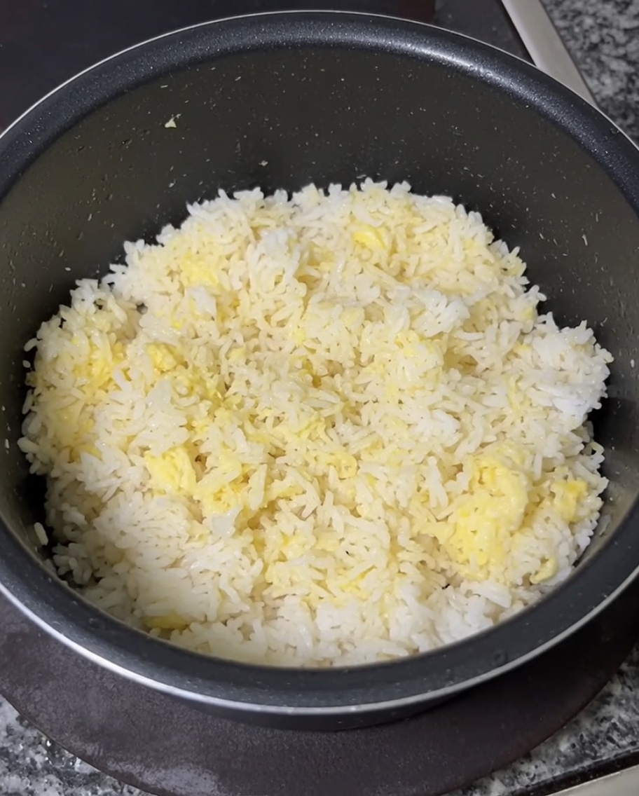 A hand using a spoon to thoroughly mix raw egg yolks into a bowl of cold white rice until evenly yellow.