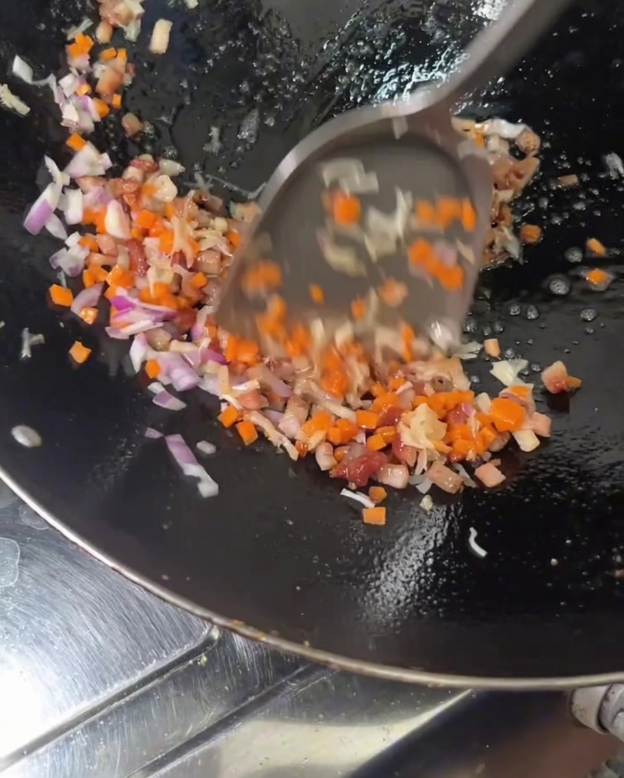Adding diced orange carrots and red onions into a hot wok filled with cooking meat and scallops.