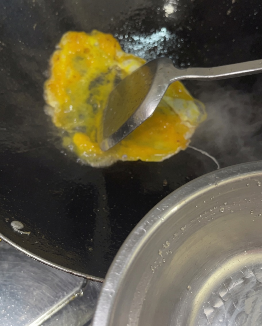 Pouring a stream of whisked raw eggs into a hot wok containing cooked vegetables and meats.