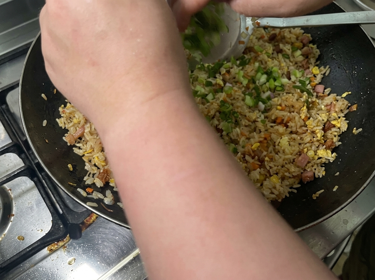 Chopped green onions being thrown into a wok filled with seasoned fried rice.
