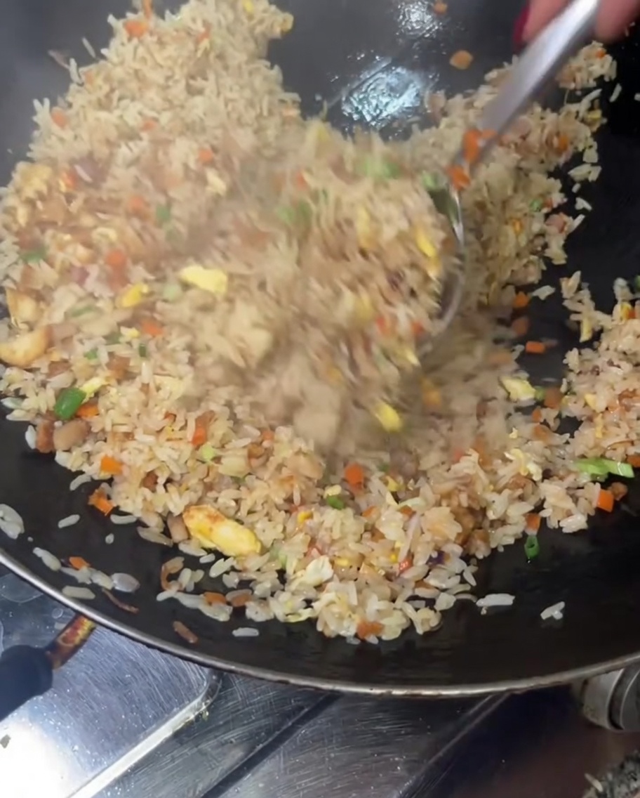 Fried rice being tossed and mixed high in a wok to combine all ingredients thoroughly.