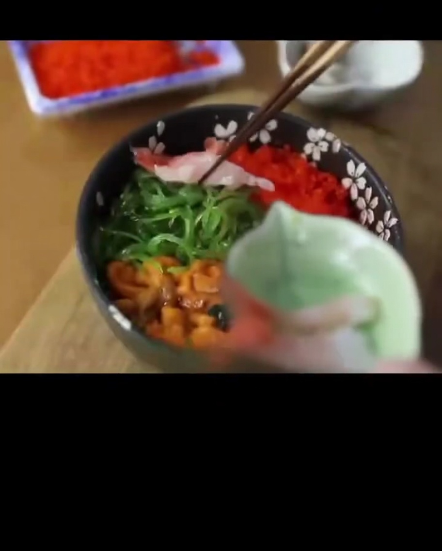 Raw, translucent sweet shrimp being placed on the side of a seafood rice bowl.