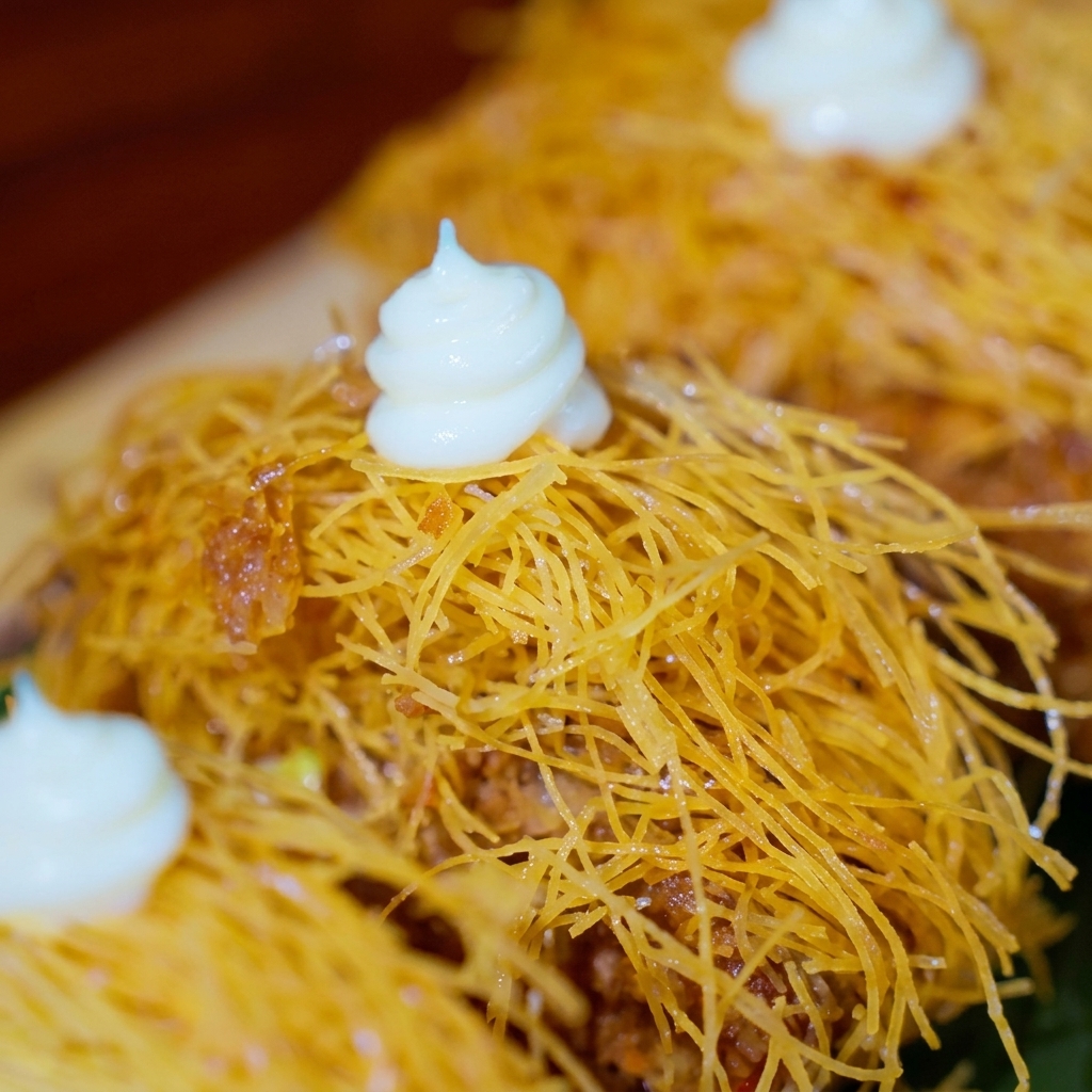 Crispy golden beef patties topped with dots of white sauce, decorated with small edible flowers and tiny red tomato wedges.