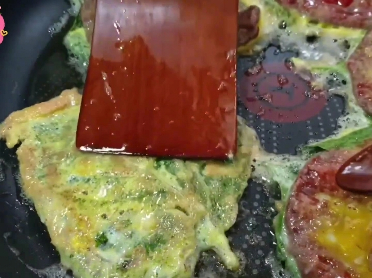 A wooden spatula flipping a golden-brown beef pancake in a hot frying pan.