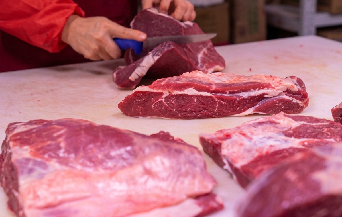 Hands using a sharp knife to slice red meat on a white cutting board.