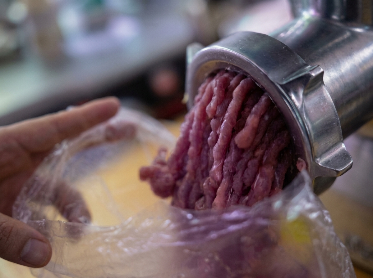 Ground meat being extruded from a mechanical meat grinder into a plastic bag.