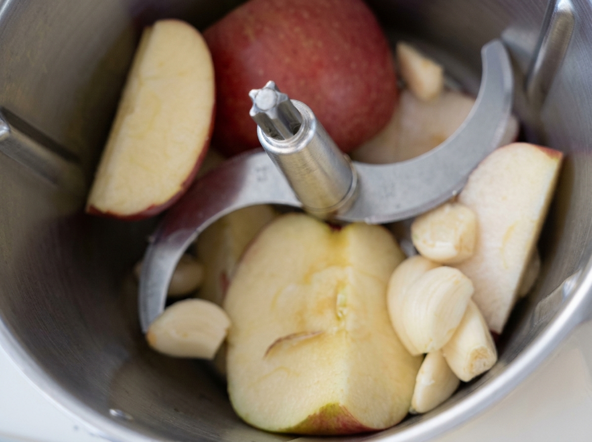 Apple slices and peeled garlic cloves inside a food processor bowl before blending.