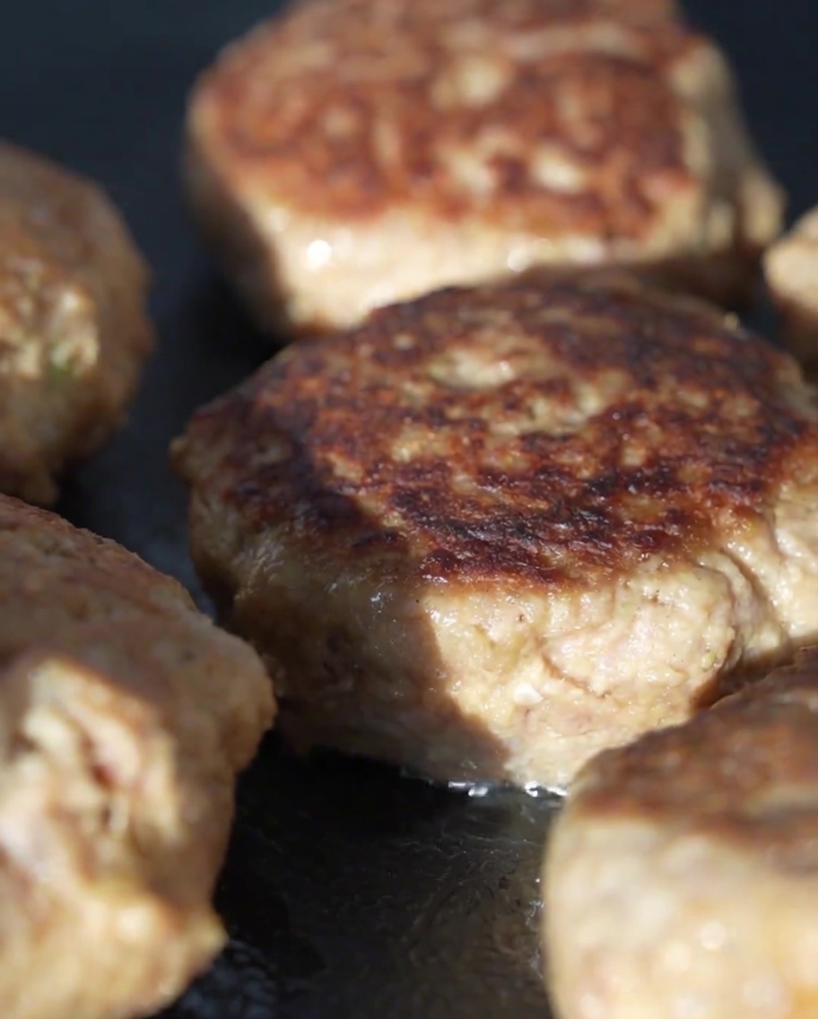 Glass lid covering the pan with meat patties inside to steam them.