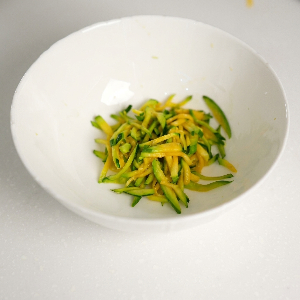 Fresh minced beef being added to the bowl containing the drained zucchini strips.