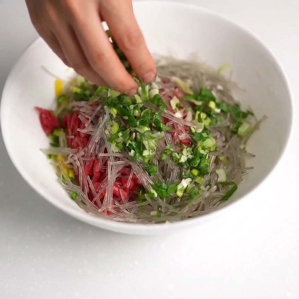 A bowl containing beef, zucchini, noodles, green onions, oyster sauce, and three cracked raw eggs.
