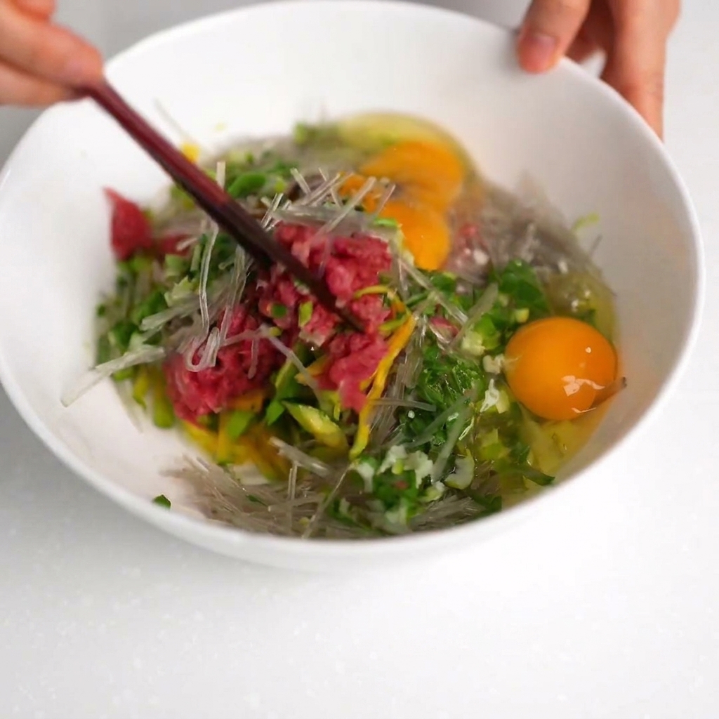 A mixture of beef, zucchini, and noodles being stirred with chopsticks in a white bowl.