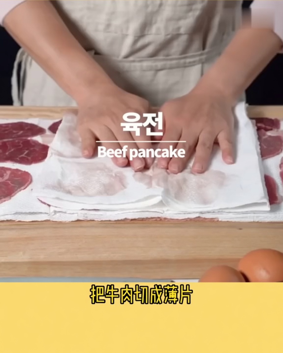Thinly sliced raw beef arranged neatly on paper towels, being brushed with a light layer of sesame oil.