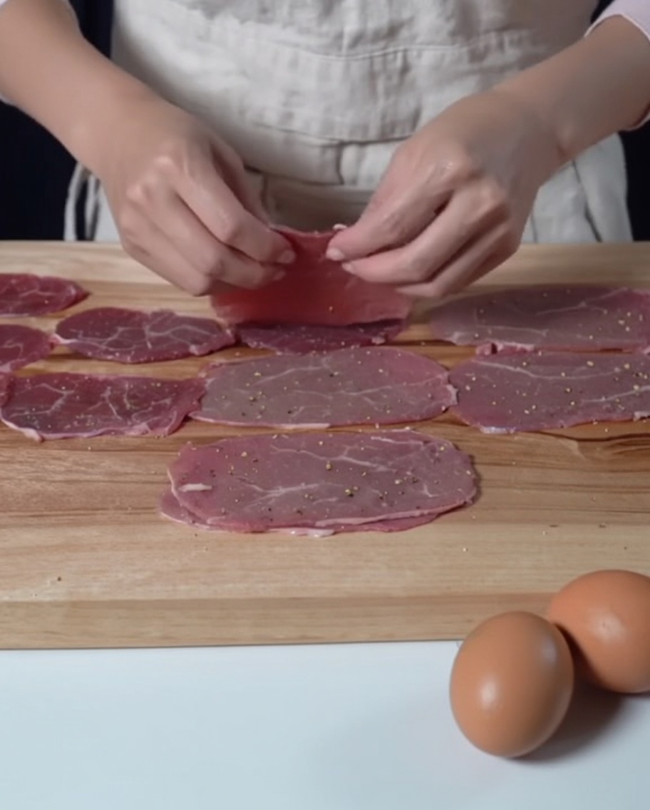 Seasoned thin beef slices laid out on a wooden cutting board, ready for the next step of flouring.