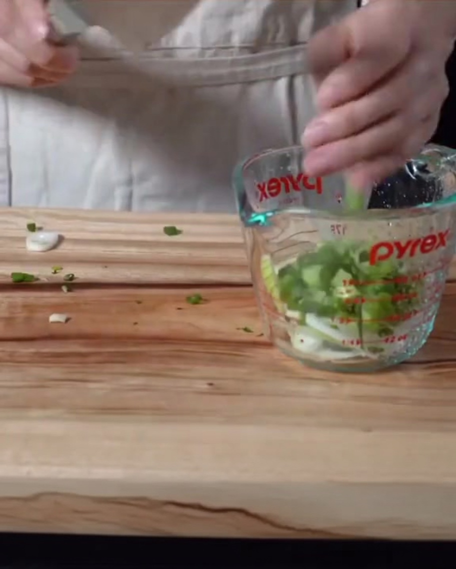 Chopped green onions and sliced onions being stirred into a dark sauce mixture inside a glass Pyrex measuring cup.
