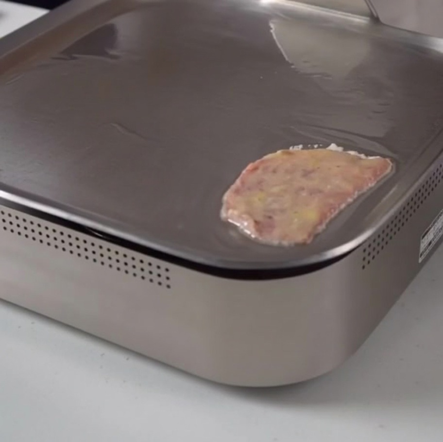 A slice of egg-coated beef cooking gently on a sleek, flat electric griddle.