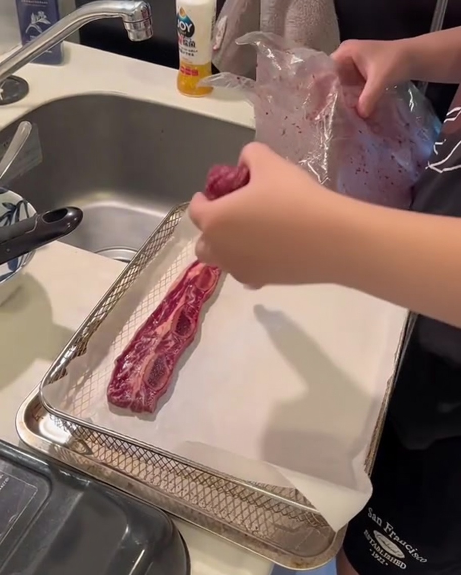 Raw flanken-style short ribs neatly arranged on a sheet of parchment paper inside an air fryer basket.