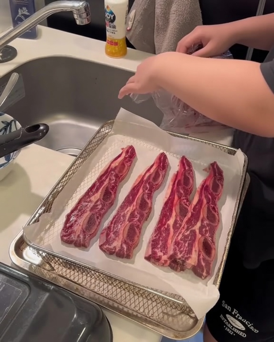 A close-up of hands using a paper towel to press down on raw beef short ribs to absorb surface moisture.