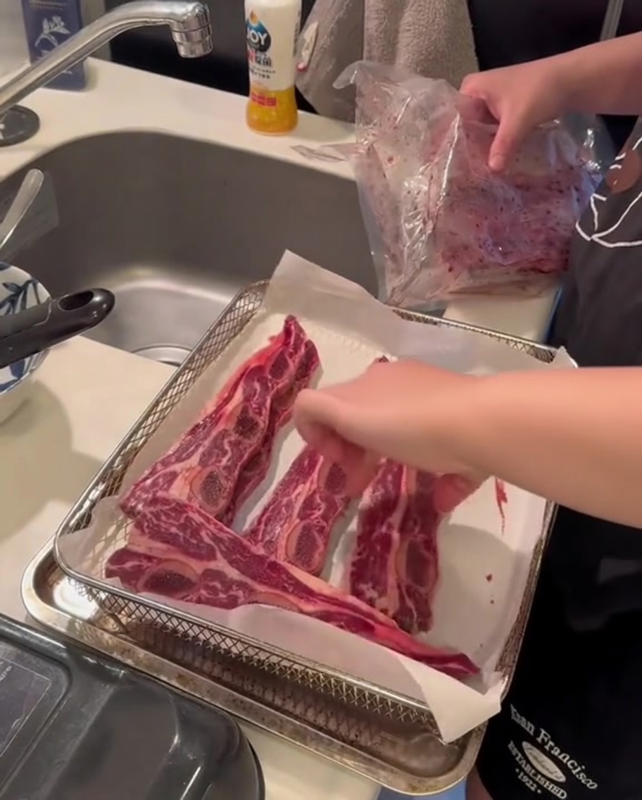 Raw beef short ribs positioned inside an air fryer basket, ready for the cooking process.
