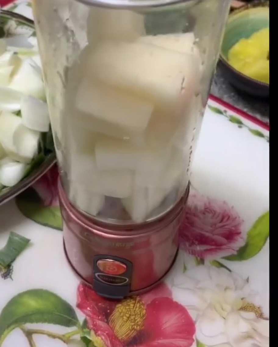 Chunks of white pear and onion stacked inside a clear blender canister.