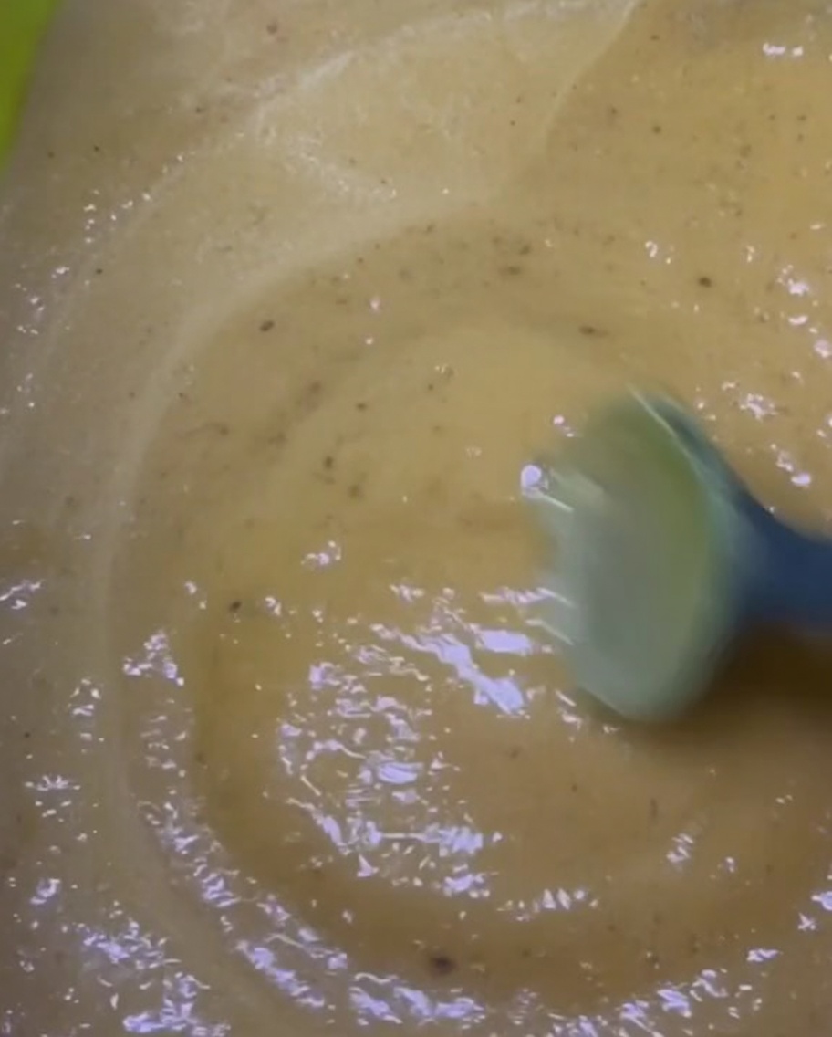 Stirring a thick, yellowish-brown marinade mixture in a bright green bowl.