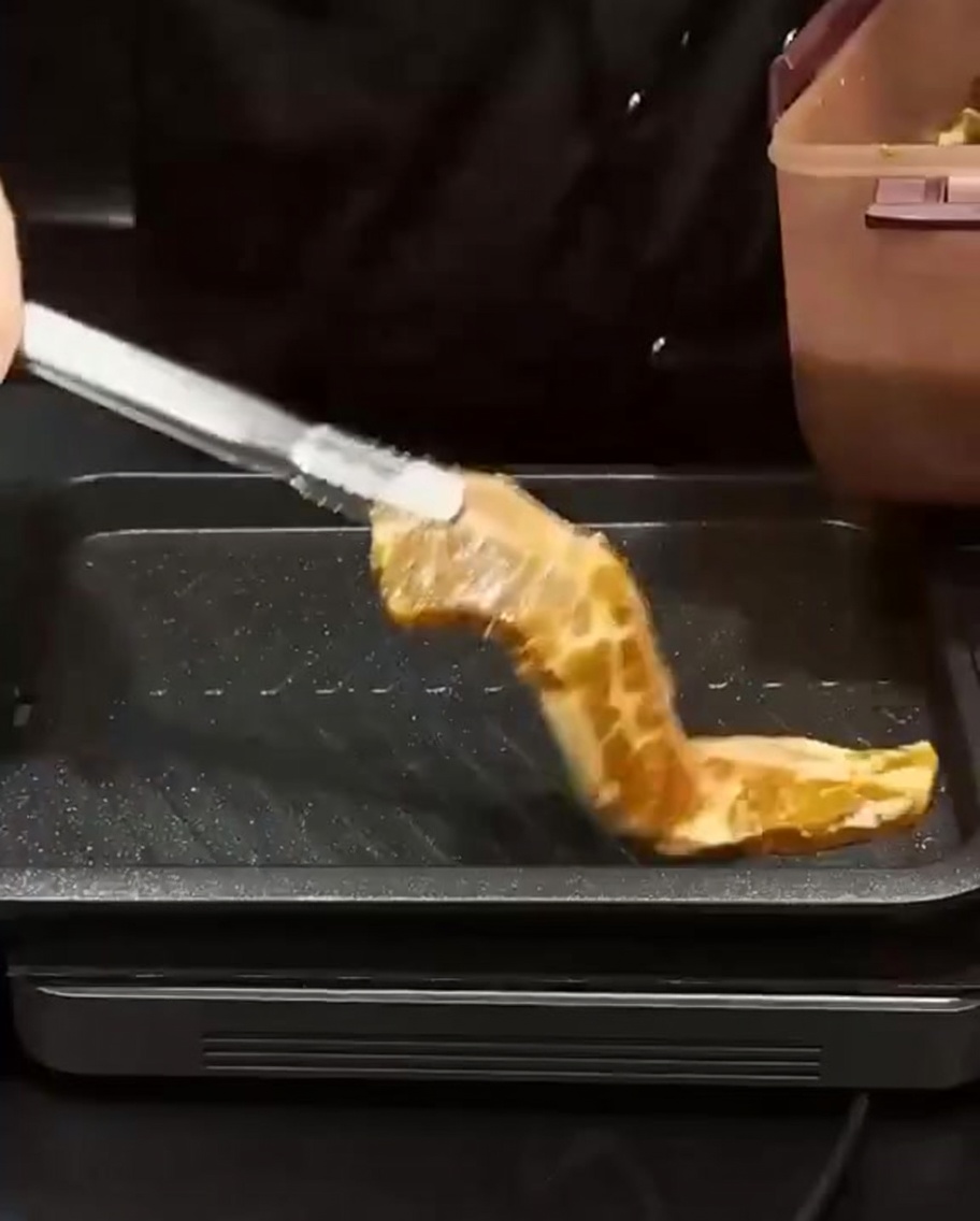 Marinated ribs being placed with tongs onto a hot rectangular grill pan to sear.
