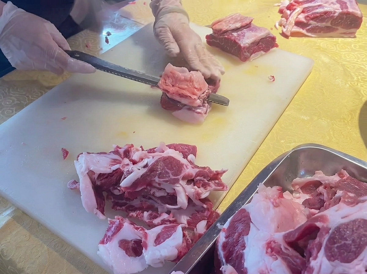 Hands using a knife to trim excess fat from a fresh cut of beef rib on a white cutting board.