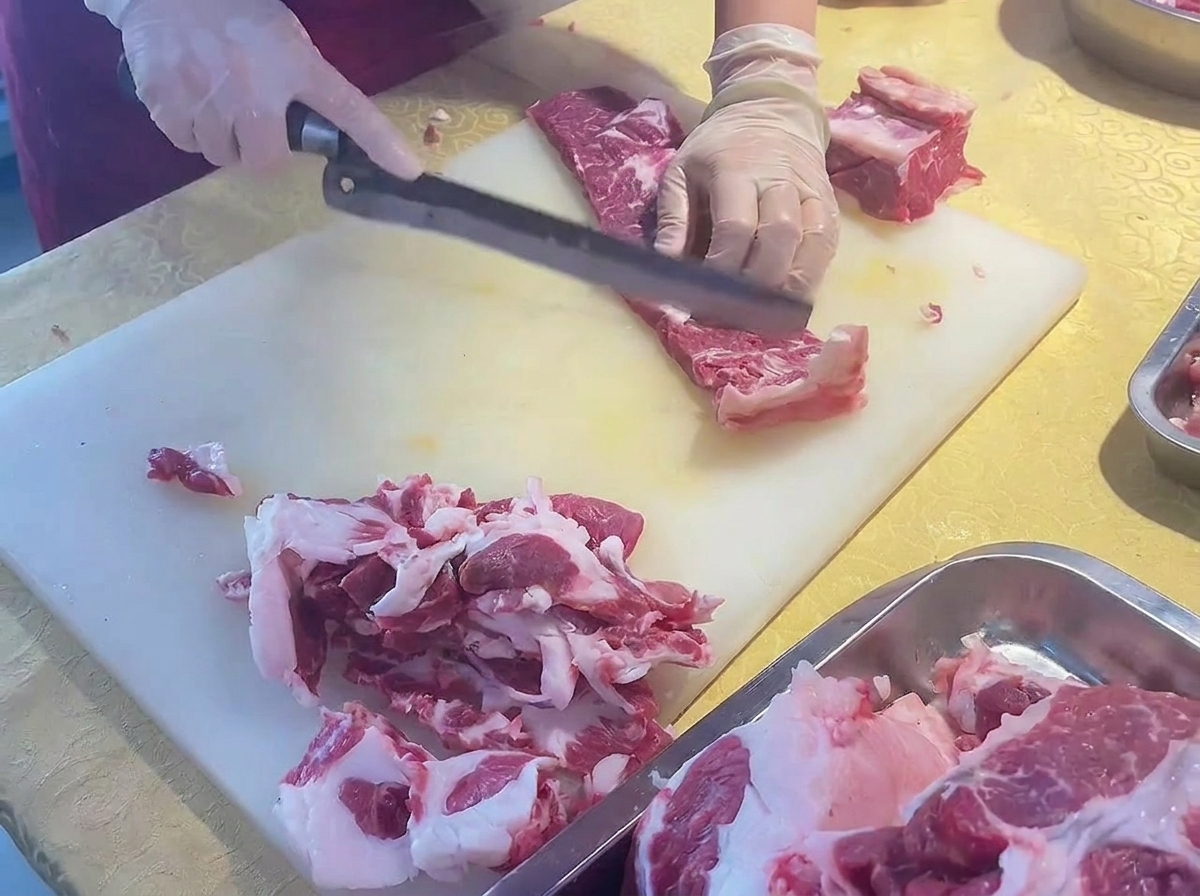 Hands slicing a trimmed beef rib into thin pieces using a long knife at an angle.