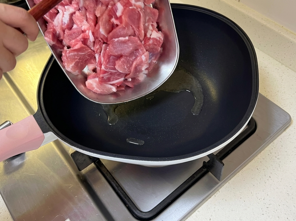 Thinly sliced pork being added to a hot pan containing shimmering oil.