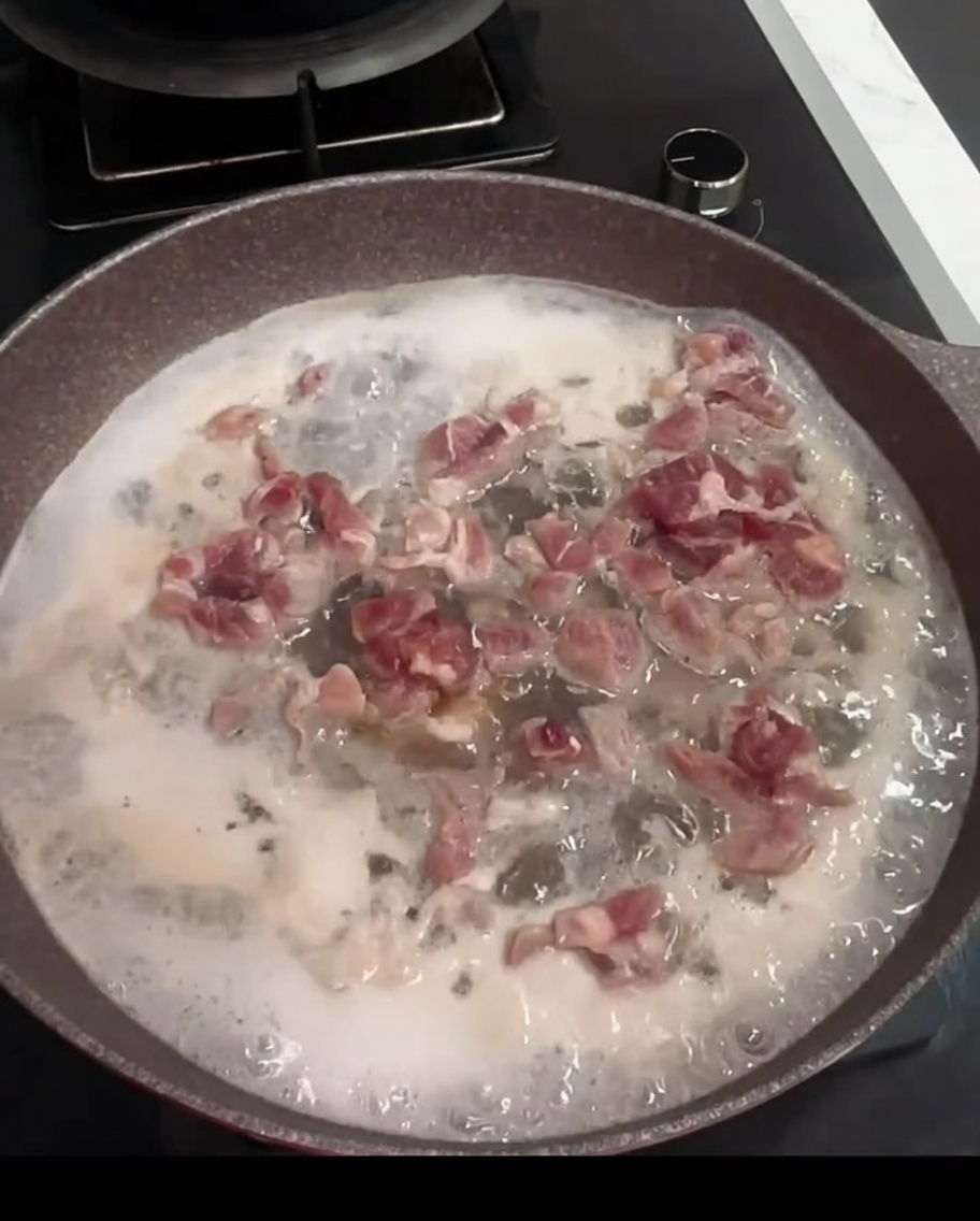 Pork pieces boiling in a pan with water, cooking wine, and a bay leaf.