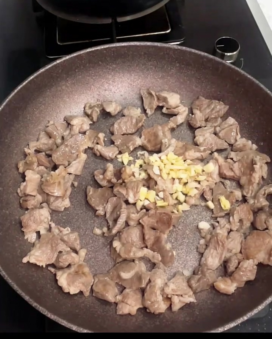 Pork pieces being stir-fried in a pan with freshly added minced garlic.