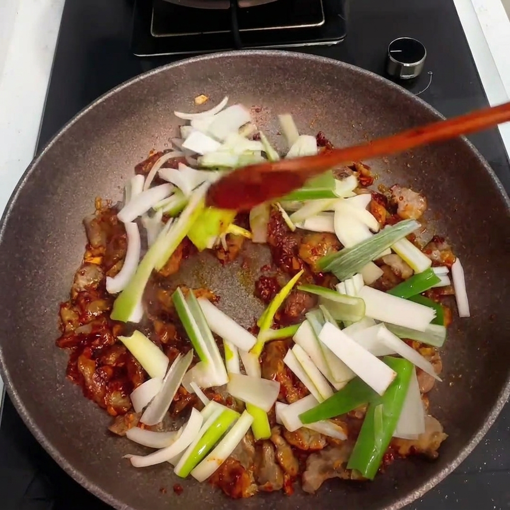 Freshly chopped onions and green onions being added to the pan with pork and sauce.