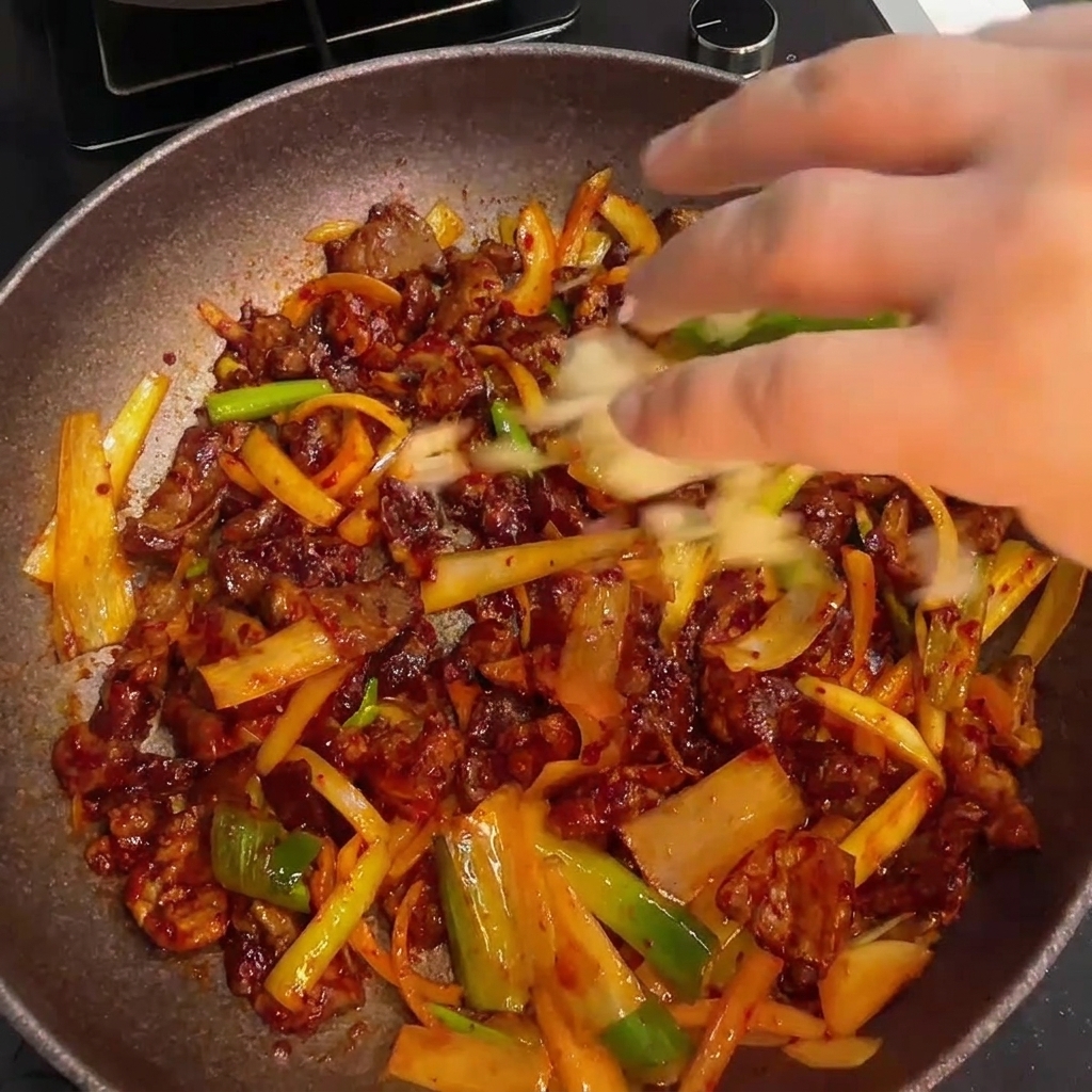 Finishing the spicy stir-fried pork by mixing in fresh minced garlic and a drizzle of sesame oil.