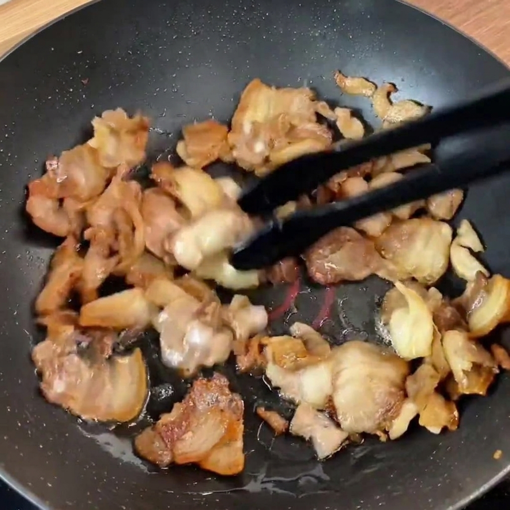 Freshly added green bell pepper strips and purple onion slices resting on top of the seared pork belly in the pan.