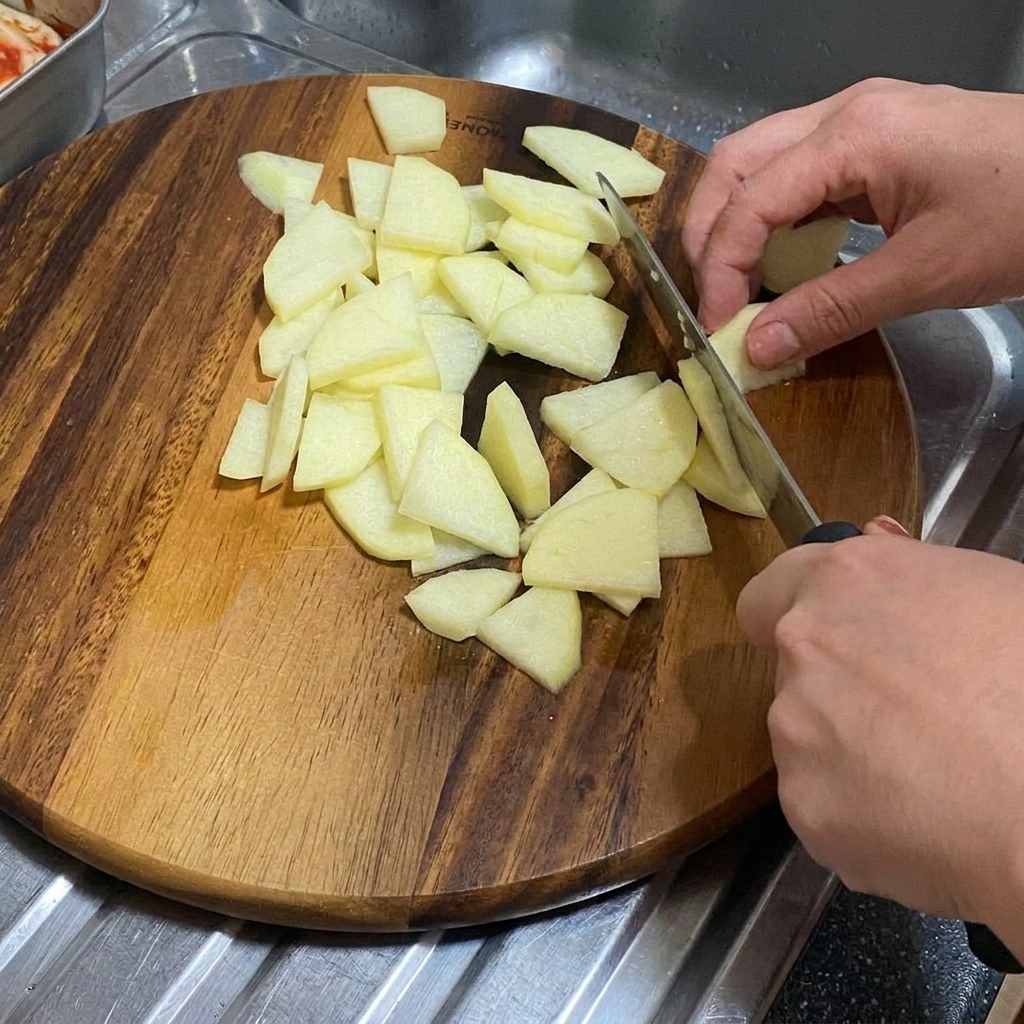 An onion being sliced into thick wedges on a wooden cutting board.