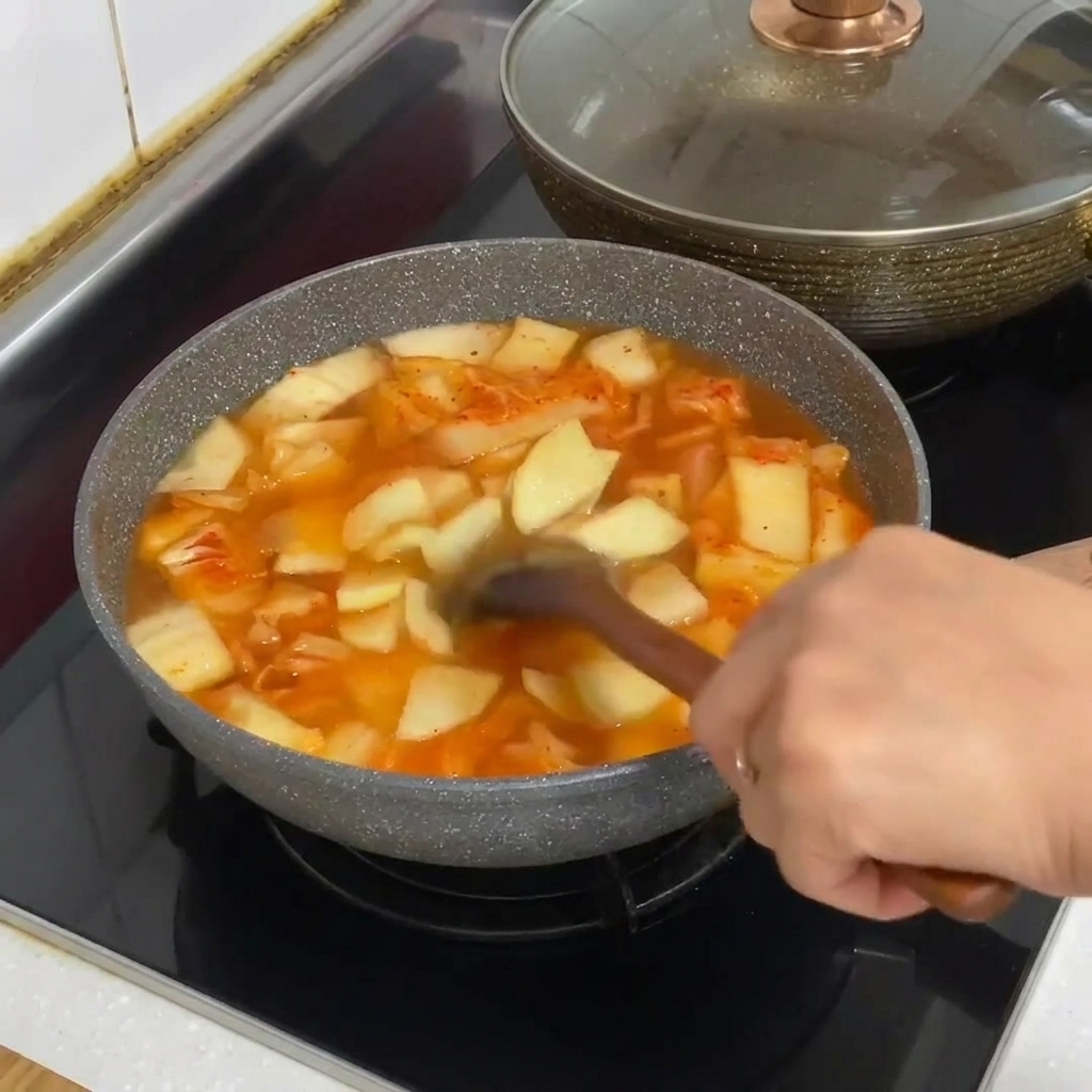 Glass noodles being added to the pot of bubbling kimchi stew.