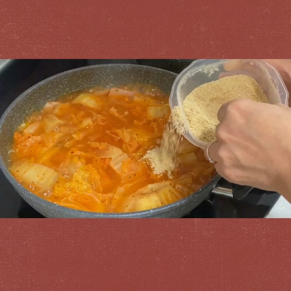 Sugar being sprinkled from a container into the simmering kimchi stew.