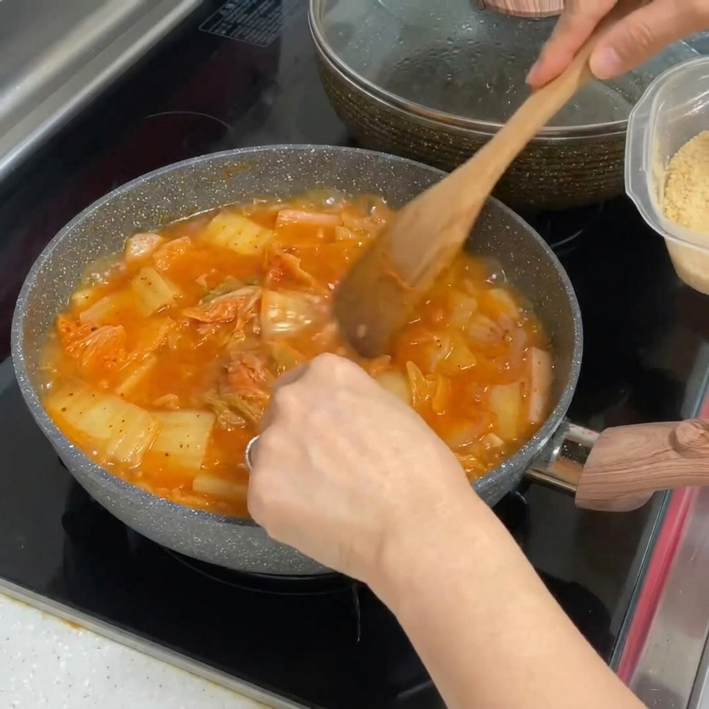 Minced garlic being stirred into a pot of vibrant, red bubbling kimchi stew.