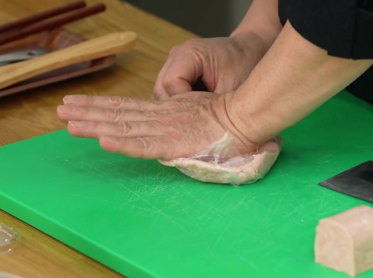 A hand pressing down on a plastic bag containing half a block of Spam to mash it into a paste.