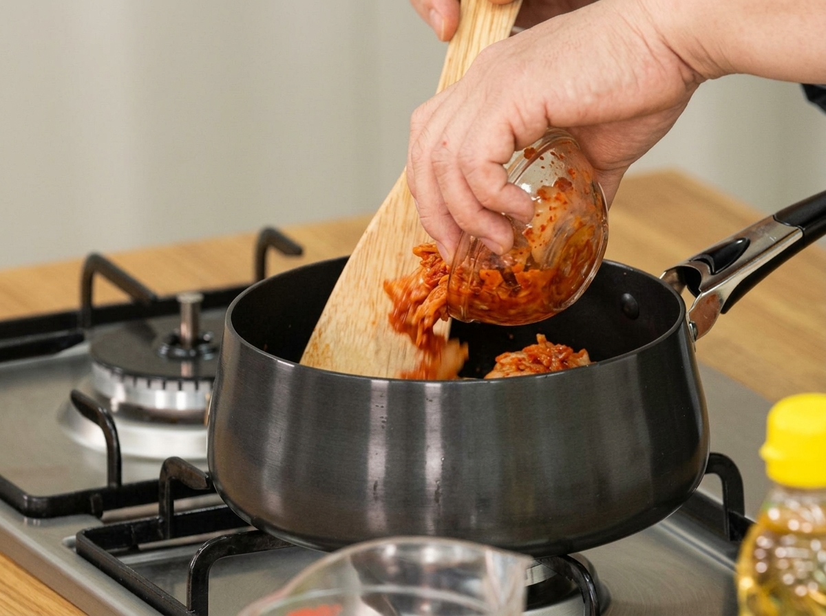 Aged kimchi being added to a pot with a wooden spoon for sautéing.