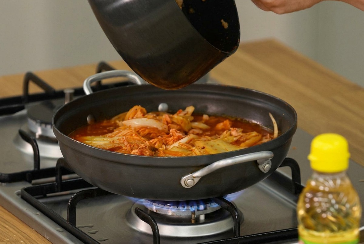 Slices of soft tofu and fresh green scallions being carefully layered over the surface of the simmering kimchi stew.
