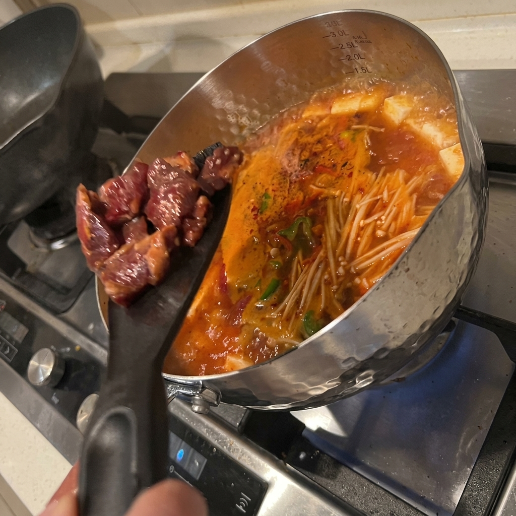 Marinated pieces of beef being dropped into the simmering pot of kimchi tofu soup.