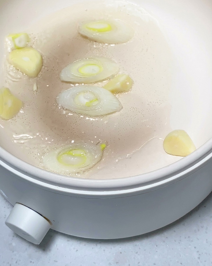 Potato chunks, minced garlic, and ginger being sautéed in a lightly oiled pan.