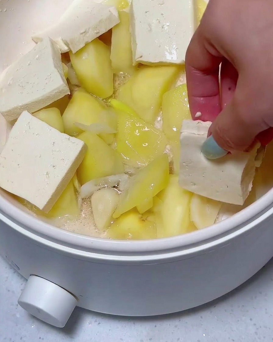 Layered slices of tofu and luncheon meat sitting atop potato chunks in the pan.